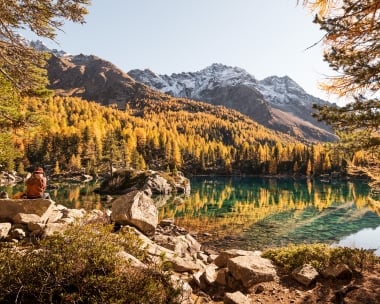 Eine Frau sitzt am idyllischen Bergsee umgeben von herbstlichen Bäumen