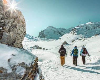 Tre escursionisti invernali in un paesaggio montano innevato sotto un cielo blu.