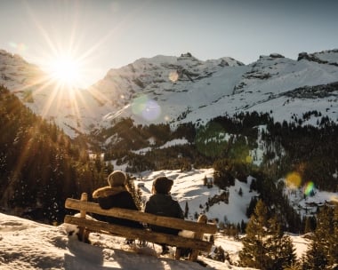 2 randonneurs en raquettes assis sur un banc avec vue sur les montagnes au coucher du soleil