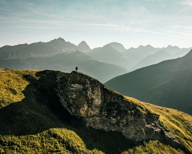 Una persona è in piedi su una roccia e ammira la valle all'alba, con un panorama montuoso sullo sfondo.