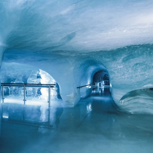 Eine beleuchtete Eishöhle mit glatten, blauen Wänden und einem Durchgang.